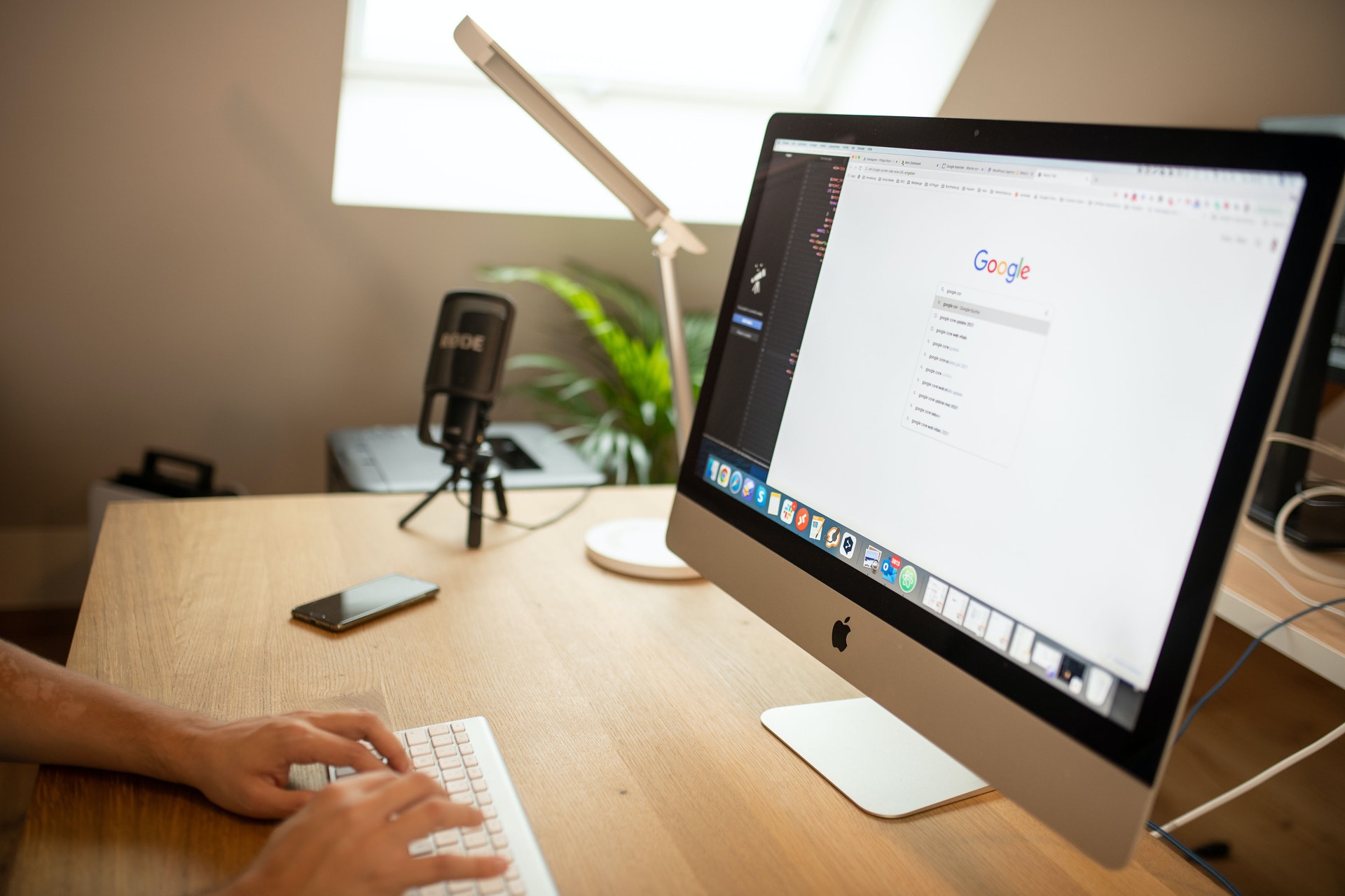 person searching Google on a mac with a phone and microphone on their desk